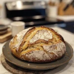 A moist slice of sourdough discard banana bread with a golden crust, served on a wooden board surrounded by bananas and nuts.